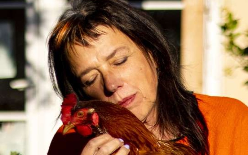Photo of a person in a green top with a chicken on his arm.