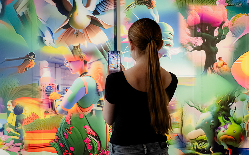 Eine Person mit Smartphone fotografiert eine bunte Bildwand.