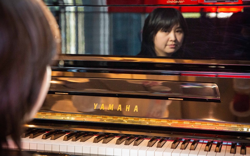 A piano can be seen, reflecting the face of a person.