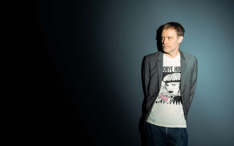 A person is standing with their arms crossed behind their back against a grey background.