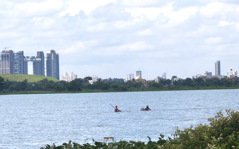 Plurality of Water, 2025 / © EKW Fishing, Avid Dabdas People in a river, skyscrapers in the background.