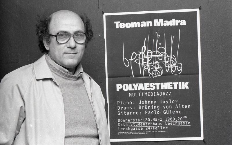 A person wearing glasses is standing next to a poster. 