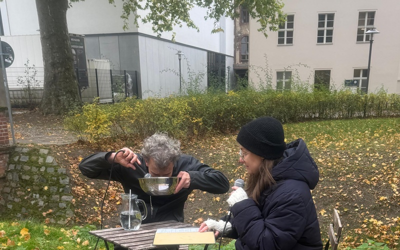 Zu sehen sind zwei Personen, die zusammen an einem Tisch im Freien sitzen. 