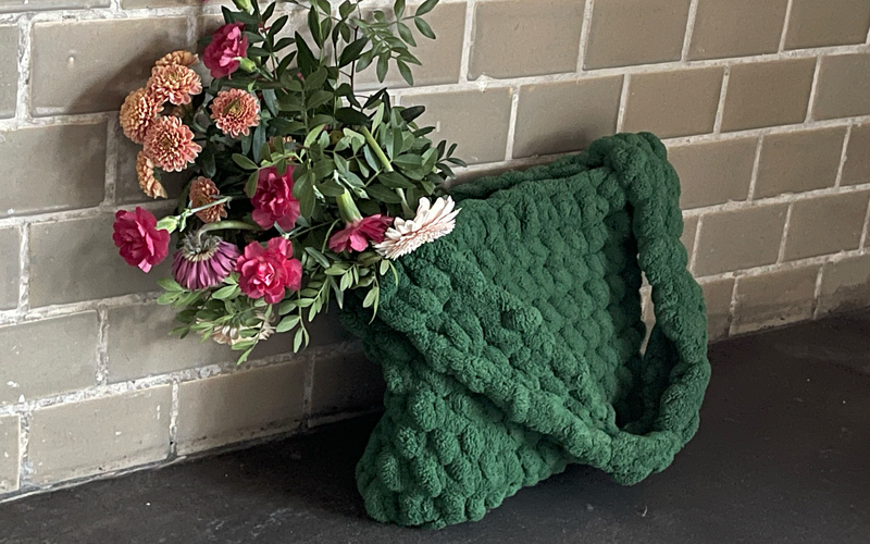Eine grüne gehäkelte Tasche mit Blumenstrauß