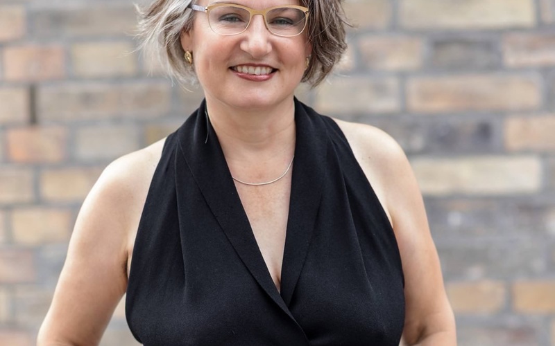 A picture shows a person standing with their hands in their pockets, smiling at the camera.