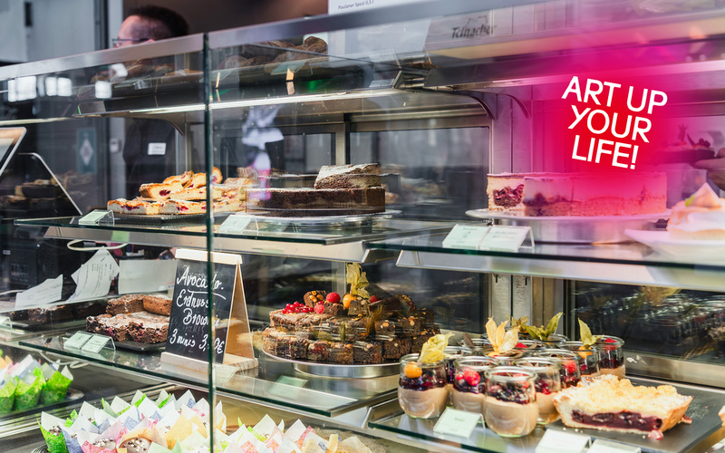 Zu sehen ist eine Theke mit verschiedenen Angeboten wie Kuchen und Muffins.