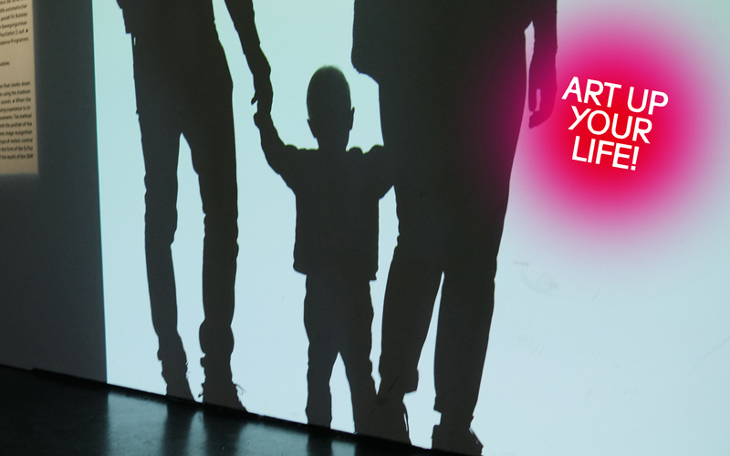 Schatten eines Kindes, das die Hände zweier Erwachsenen hält vor weißem Hintergrund.