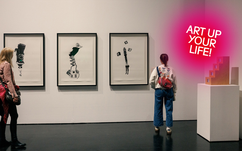 Mehrere Menschen schauen sich eine Bildserie an einer Wand in einem Ausstellungsraum an.