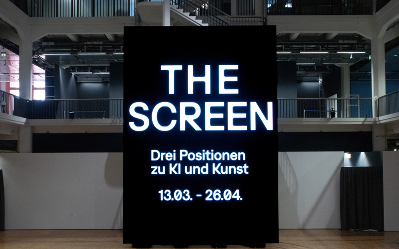 Ein riesiger Bildschirm mit dem Schriftzug "THE SCREEN. Drei Positionen zu KI und Kunst".