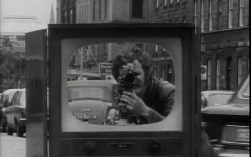 Zu sehen ist eine Schwarz-Weiß-Aufnahme, die einen Fernseher auf einer Straße zeigt.