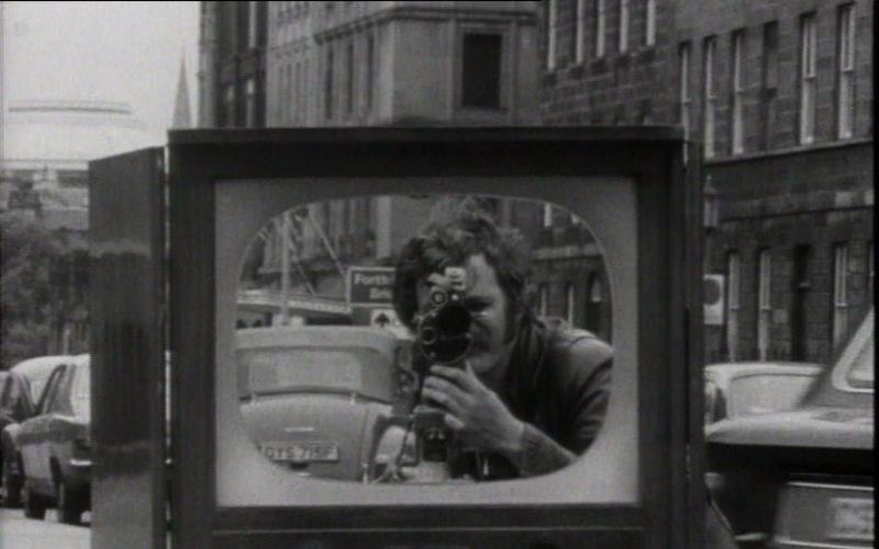 Zu sehen ist eine Schwarz-Weiß-Aufnahme, die einen Fernseher auf einer Straße zeigt.