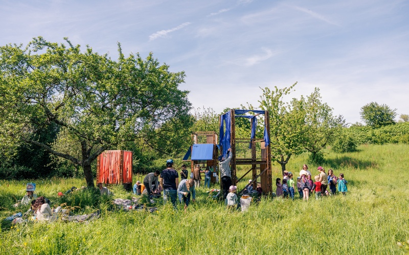 Kinder und Erwachsene auf einer Wiese mit Bäumen.  