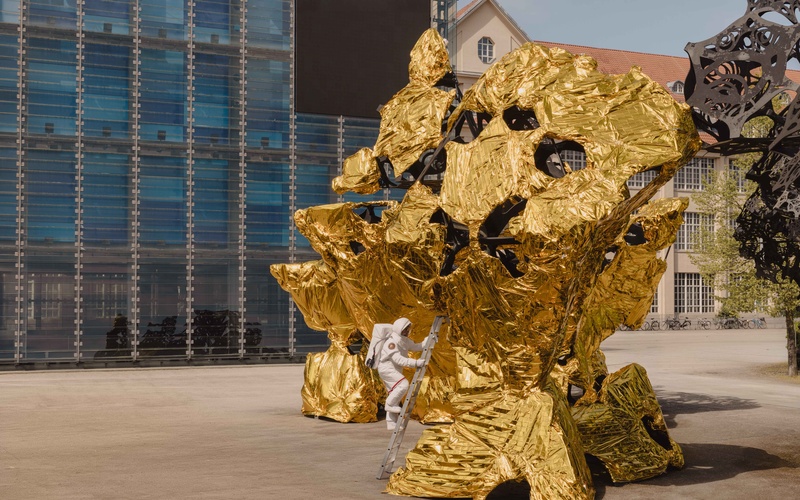Ein Astronaut steigt vor dem ZKM Karlsruhe aus einem goldenen Gebilde.