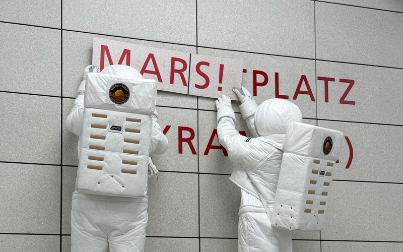 Zwei Astronaut:innen hängen ein Schild in der Karlsruher U-Bahn auf.