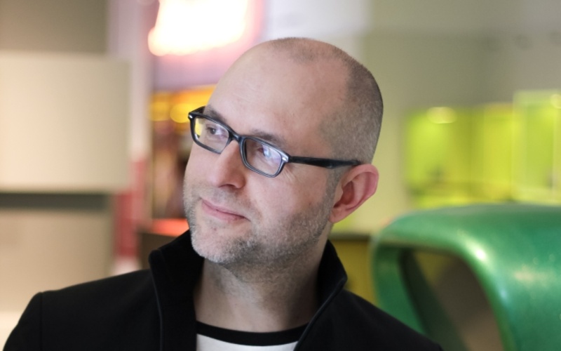 Das Bild zeit Matthias Oborski. Er trägt eine Brille und eine schwarze Jacke und guckt freundlich zum linken Bildrand