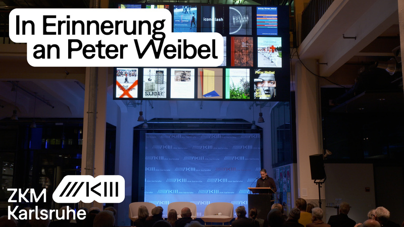 Gedenkabend für Peter Weibel, auf der Bühne steht Jens Lutz, die Projektion zeigt eine Auswahl an Publikationen