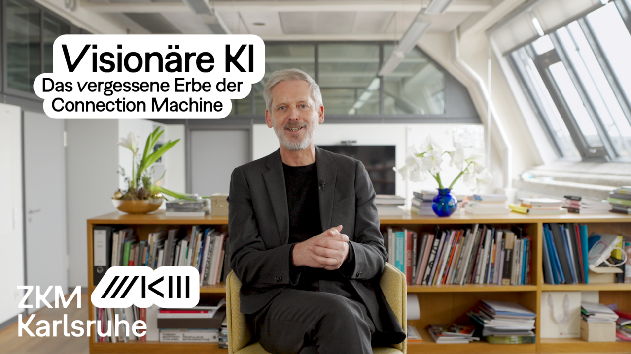 Alistair Hudson is sitting in his office. Behind him is a bookcase and a bouquet of flowers. 