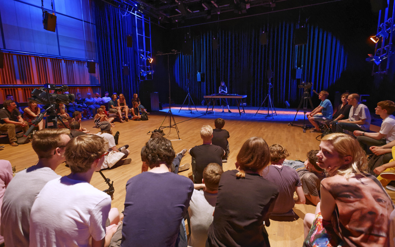 People sitting around a stage on which a woman stands.