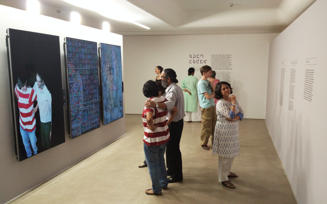A group of people is standing in an exhibition space with white walls, reading the exhibition's texts or interacting with an installation.