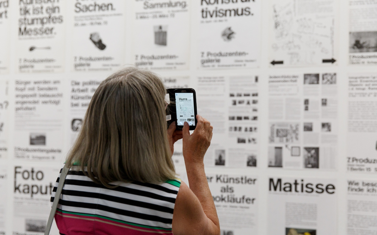 Eine Besucherin fotografiert mit Ihrem Smartphone eine Wand voller Typographie-Plakate. 