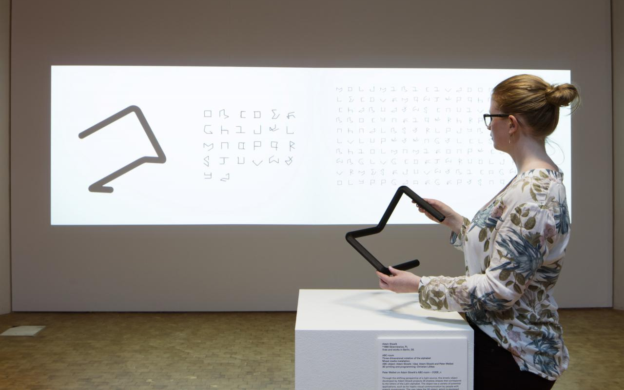 A woman holding a black object in front of a canvas with letters