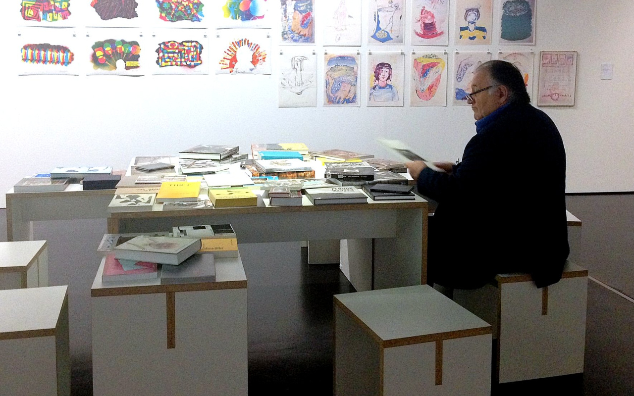Peter Weibel sitzt im ZKM an einem Tisch mit Büchern