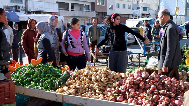 A woman is wearing headphones and dances in front of a market stall