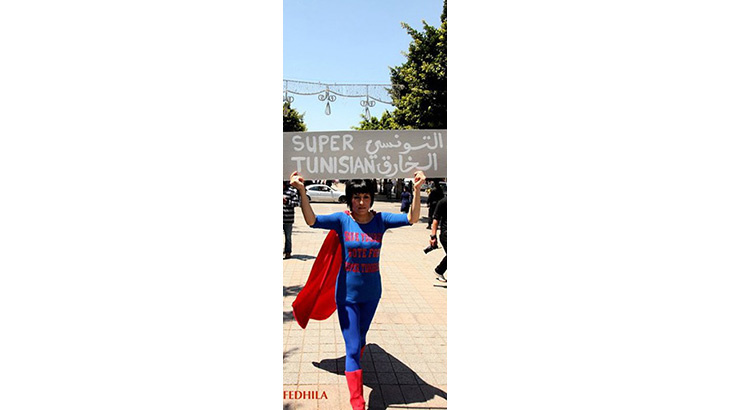 Eine Frau in einem Superman-Kostüm hält ein Schild hoch