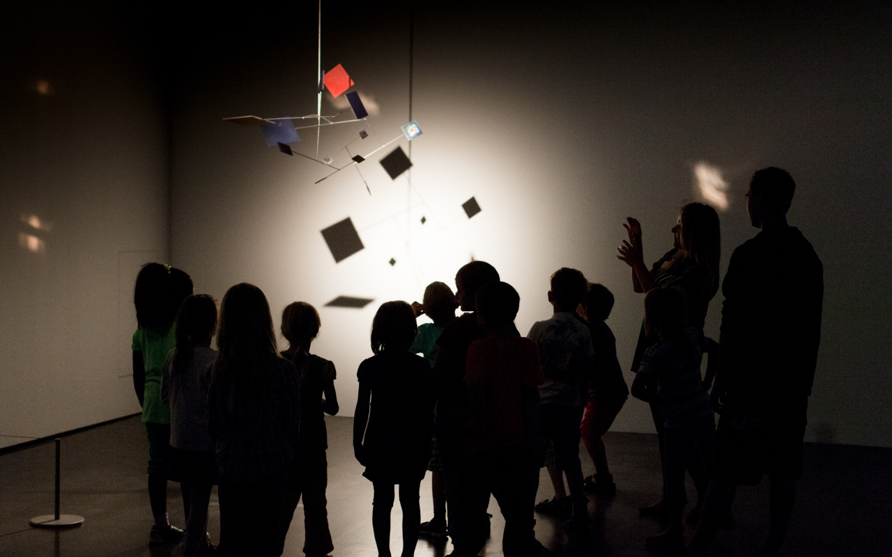 Kids are standing in the dark museum, gazing at an mobile, that is illuminated