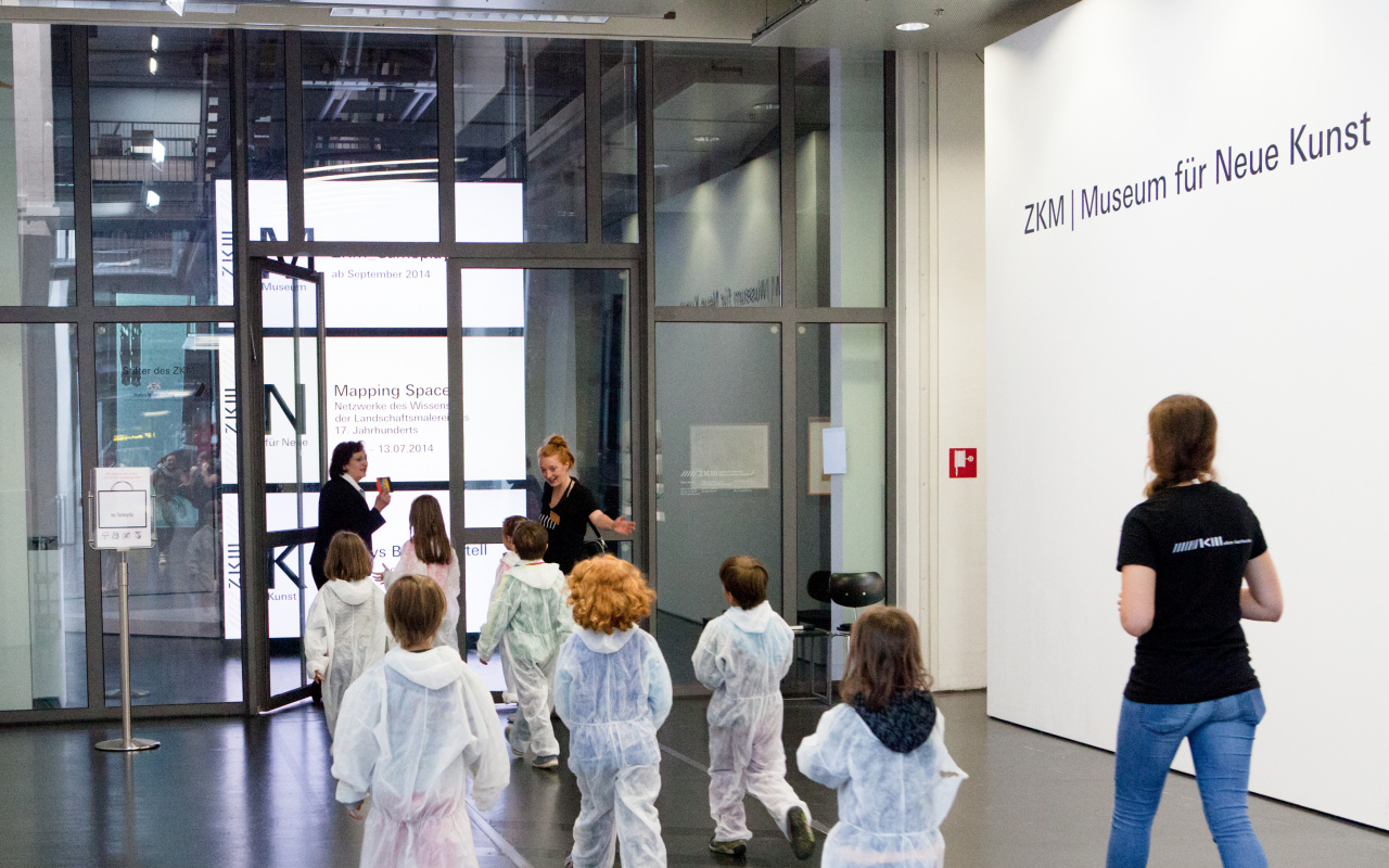 Kinder in weißen Overalls betreten das Museum für Neue Kunst