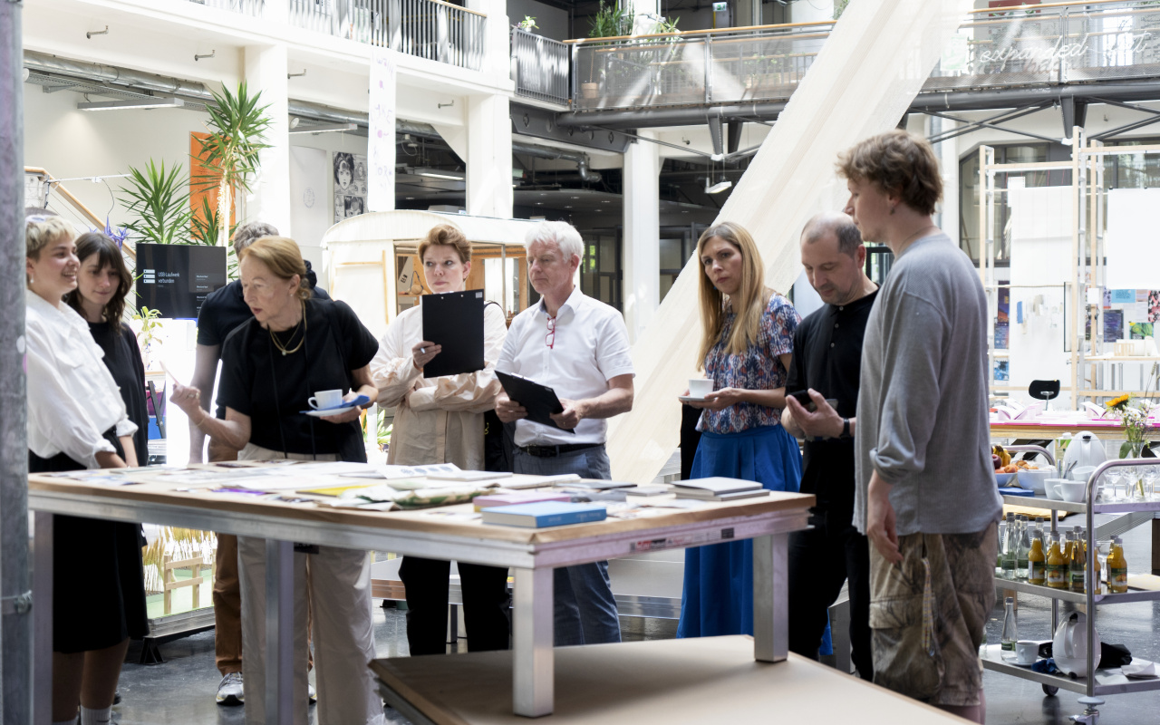 Personen mit Mappen stehen vor einem Tisch mit Büchern und diskutieren.