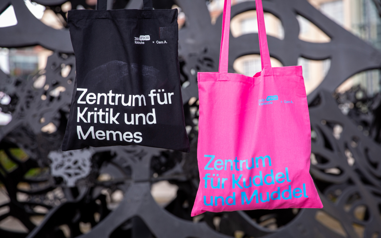 Zu sehen sind zwei Stofftaschen mit Aufschrift. 