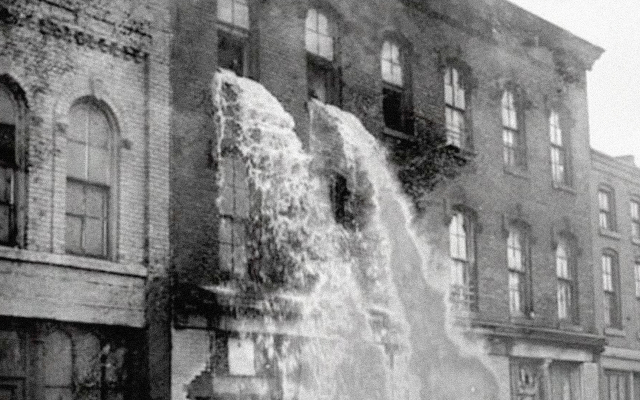 You see a factory building with a waterfall bursting out of the window in black and white.