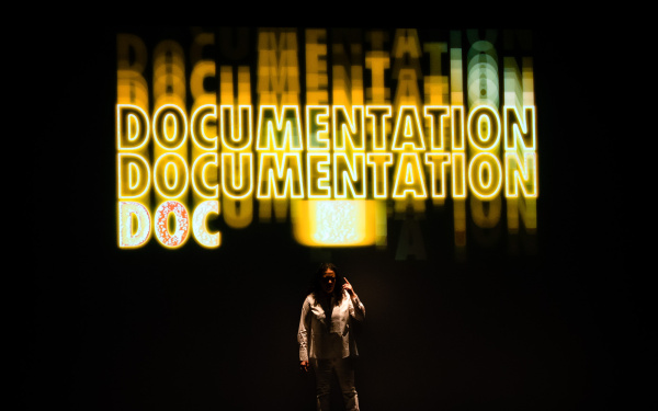 Noa Frenkel steht vor einem Hintergrund, auf dem mehrmals untereinander in groß »Documentation« geschrieben steht.