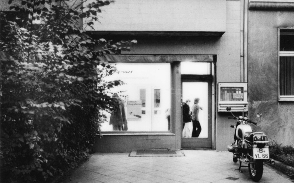 Schwarz-weiß Foto zeigt die Straßenansicht eines Galerieraum. Davor steht ein Motorrad.