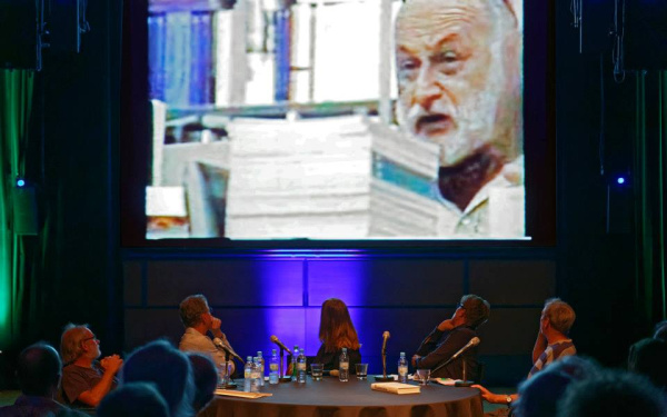 Die Diskussionsteilnehmer blicken auf eine Projektionsleinwand hinter ihnen, die ein Video mit Vilém Flusser zeigt.