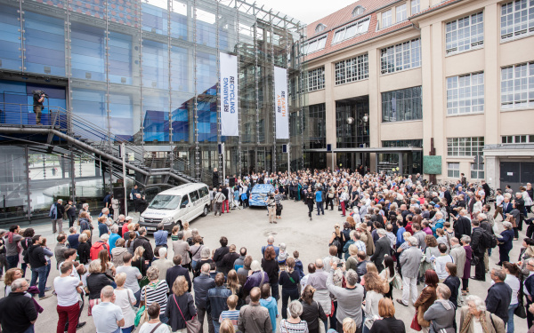 Eine Menschenmenge vor dem ZKM-Eingang versammelt sich um ein blaues Auto