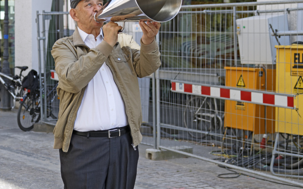 A man stands on the street with a silver megaphone
