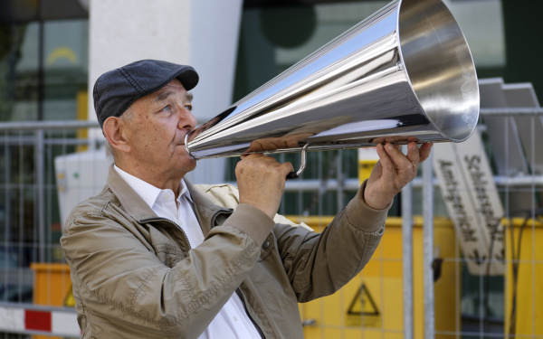 A man stands on the street with a silver megaphone