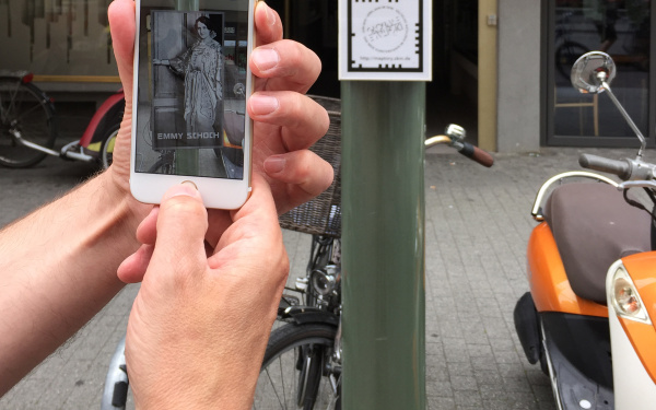 Ein Smarthphone wird hochgehalten, um den Augmented-Reality-Marker auf einer Säule zu erfassen.