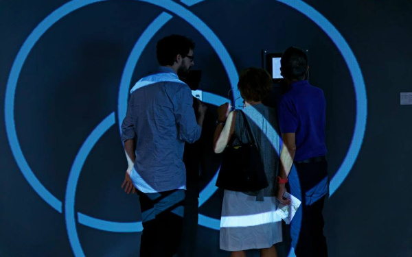 Drei Menschen stehen vor einer Wand. Auf sie werden blaue Kreise projiziert.