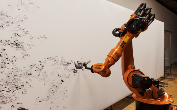 An industrial robot is drawing with pen on a large format.