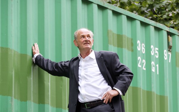 Ein Mann hängt in der Luft, hebt sich an einem Baucontainer mit nur einer Hand fest