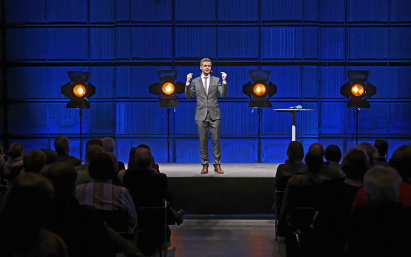 A man in a suit, standing on a stage.