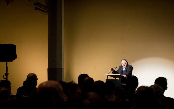 A man stands at a desk and talks to the audience