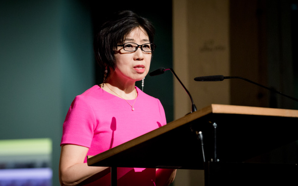 A woman dressed in a pink dress talks to the audience