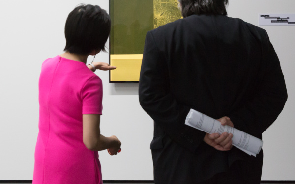 Two persons stand in front of a hanging picture