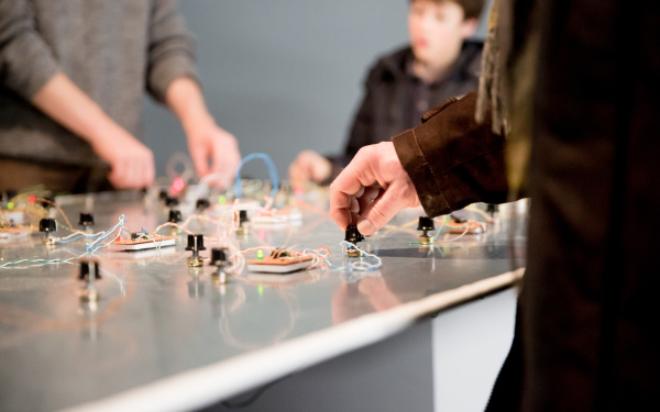 Persons turn small knobs on a desk