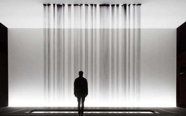 A person stands in front of a sculpture, at the drop several rivulets of oil on the floor
