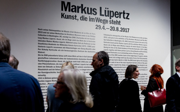 The picture shows visitors in front of an information board for Markus Lüpertz